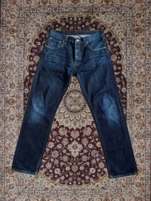 Nudie Jeans Big Bengt (discontinued) - Nudie Jeans Big Bengt Ovanlig samt eftertraktad modell som inte längre säljs. Jeansen är i Dark Crinkle wash och sparsamt använda.  Få slitningar (Se sista bilder) W33 L32 men sitter något mindre i midjan (Se mått).  Midja: 39cm Ytterben: 103cm Innerben: 77cm Benöppning: 19cm   Priset går att diskutera och hör av dig vid frågor!
