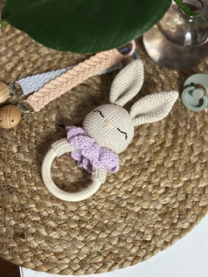 Virkad kanin skallra med trähandtag - Söt handgjord skallra i form av en beige kanin med långa öron och virkad lila krage. Kaninen har broderade ögon och näsa, och handtaget är i ljust trä. Perfekt som babyleksak eller doppresent.