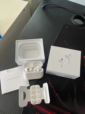 Apple AirPods Pro 3 2025 - Säljer ett par vita Apple AirPods Pro 3 2025 med trådlöst laddningsetui. Hörlurarna har silikonproppar i olika storlekar och levereras med originalförpackning och tillbehör. Snygg och stilren design i blankt plastmaterial.