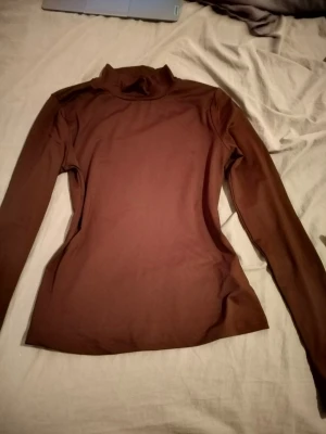 Brun polotopp i bomull - Snygg brun polotopp med lång ärm och tight passform. Tillverkad i mjuk bomull som känns skön mot huden. Perfekt att styla med jeans eller kjol för en clean look.