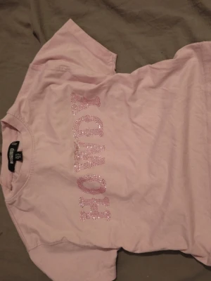 Rosa t-shirt med glittertext - Söt rosa t-shirt från H&M med glittrig text framtill. T-shirten har klassisk passform och korta ärmar. Perfekt för dig som gillar en enkel men ändå lite extra look.