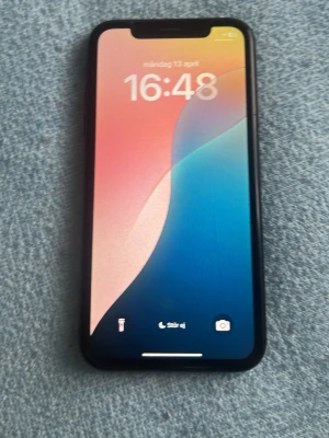 Svart iPhone XR med stor skärm - Säljer en svart iPhone XR med snygg, stilren design och rundade kanter. Telefonen har en stor LCD-skärm med tunna ramar och Face ID. Baksidan är i glas och har en enkel kamera med blixt. Perfekt för dig som gillar Apple och vill ha en modern mobil.