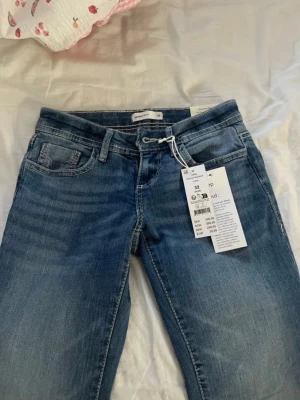 Blå ultra low flare jeans Gina Tricot - Säljer ett par blå jeans från Gina Tricot med ultra low waist och flare ben. Klassisk femficksmodell med snygg tvätt och trendig passform. Perfekta för dig som gillar 00-talsvibbar och vill ha ett par riktigt schyssta jeans i garderoben. Helt nya med prislapp. Nypris 399kr men säker pga att de är för små i midjan. Jag är 168 cm och de passar mig i längden 