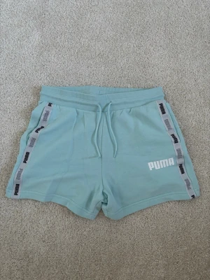 Puma shorts - Snygga ljusblå/turkosa shorts från Puma med vita loggor längs sidorna och snörning i midjan. De är väldigt sköna till sommaren och i ett bra skick.