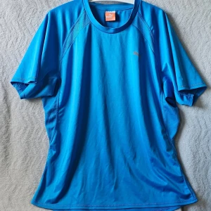 Blå tränings-tshirt från Puma - Säljer en blå tränings-tshirt från Puma med rund hals och korta ärmar. Materialet är lätt och andas, perfekt för sport och gym. Diskret Puma-logga på bröstet. Snygg passform och sportig look.