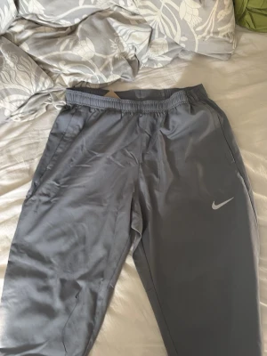 Grå Nike byxor - Snygga grå mjukisbyxor från Nike med elastisk midja och diskret logga på benet. Byxorna har raka ben och sidofickor, perfekta för chill eller träning. Materialet är mjukt och lätt, vilket gör dem riktigt bekväma att ha på sig.