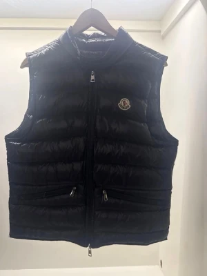 Svart dunväst från Moncler - Snygg svart dunväst från Moncler med hög krage och tvåvägsdragkedja framtill. Den är äkta ja har kvitto.