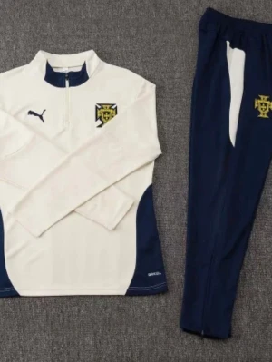 Puma träningsset i vitt och marinblått - Snyggt träningsset från Puma med långärmad vit tröja och marinblå detaljer samt matchande marinblå byxor. Tröjan har halv dragkedja, klubbmärke på bröstet och Puma-logga. Perfekt för fotbollsträning eller gymmet.