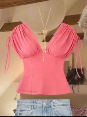 SÖKER!!!! - Trendig rosa topp med omlottdesign och snörning på axlarna. Toppen har djup v-ringning och är ärmlös, vilket ger en feminin och somrig look. Passformen är figurnära och materialet känns mjukt och bekvämt.