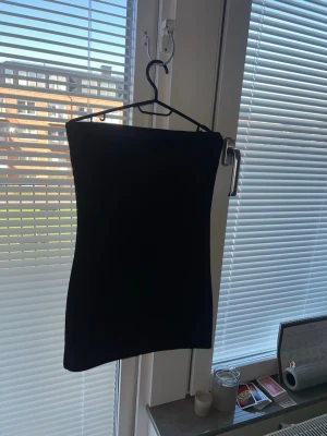 Svart axelbandslös kort klänning, Gina Tricot  - En stilren svart axelbandslös kort klänning med tight passform. Perfekt för dig som gillar minimalistisk och klassisk stil. Enkel att matcha med accessoarer och passar till många olika tillfällen.