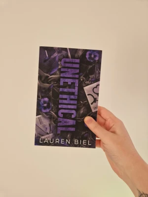 Unethical av Lauren Biel - En mörk och spännande pocketbok med titeln 'Unethical' av Lauren Biel. Omslaget är svart med lila detaljer, blommor och mystiska element som anteckningar och kedjor. Perfekt för dig som gillar psykologiska thrillers och intensiv skönlitteratur. Nypris 182 kronor