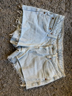 Ljusblå low waist jeansshorts från Levi's - Säljer ett par ljusblå jeansshorts från Levi's med fransiga benslut och klassisk femficksdesign. Shortsen är lågmidjade och är i storlek 26W. 