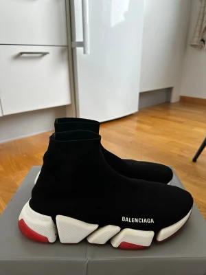 Balenciaga Speed Trainer svarta sneakers - Äkta! Köpt för 9 800kr på Luisaviaroma digitalt kvitto finns samt box och papper! Svarta Balenciaga Speed Trainer sneakers med stickad ovandel i textil, vit och röd sula samt logga på sidan. Strumpliknande passform som sitter tajt runt foten och ger en futuristisk vibe. Perfekta för dig som gillar streetwear och vill sticka ut.