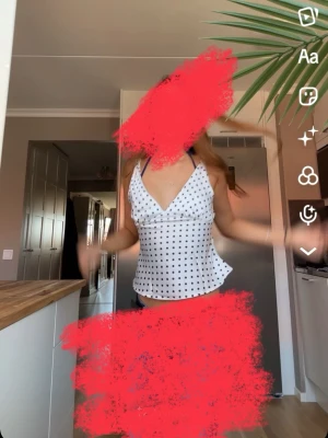 Vit prickig omlottopp med v-ringning - Snygg vit omlottopp med svarta prickar och djup v-ringning. Toppen har smala axelband och knyt i sidan för en feminin look. Perfekt till jeans eller kjol för en trendig stil.