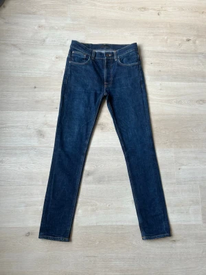 Blåa Dry Nudie Lean Dean Jeans Storlek W32 L32 - Mycket fina Nudie Jeans i blå färg. Jeansen är i mycket bra skick och sparsamt använda. |  Äkta som allt annat jag säljer! ✅ |  Storlek: W32 L32 | Skick: Mycket Bra Skick | Färg: Blå | Märke: Nudie | Modell: Jeans |   Hör gärna av dig vid frågor så svarar jag så fort jag kan! 😁 |  (SKU - 119)