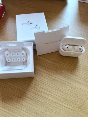 Apple AirPods Pro med laddningsetui - Säljer ett par Apple AirPods Pro i vit färg med tillhörande laddningsetui och extra silikontoppar. Hörlurarna har en stilren och kompakt design med rundade former och levereras i originalförpackning. Perfekta för musik, samtal och vardagslyssning.