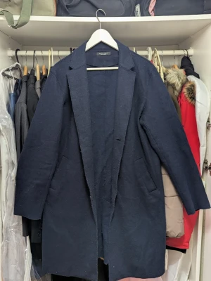 Mörkblå ullrock från Zara Man - Stilren mörkblå rock från Zara Man i ullblandning. Klassisk rak modell med slag, två sidofickor och enkel design utan synliga knappar. Perfekt för dig som vill ha en tidlös och snygg look.