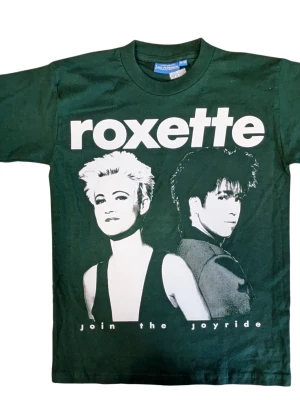 150cl. Grön Roxette t-shirt med tryck - Barntröja 150-160 cl. Cool grön t-shirt med stort Roxette-tryck och texten 'Join the Joyride' på framsidan. Klassisk passform med rund hals och korta ärmar. Perfekt för dig som gillar bandtröjor och vill sticka ut med en retrostil.