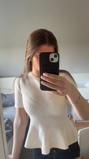 Vit ribbad peplumtop - Snygg vit ribbad peplumtop med rund halsringning och korta ärmar. Toppen har en figurnära passform upptill och en utsvängd nederdel som ger en feminin siluett. Perfekt att styla med jeans eller kjol för en trendig look.