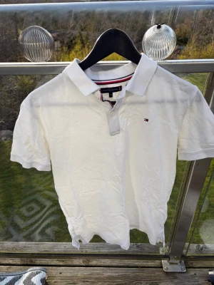 Vit piké från Tommy Hilfiger - Klassisk vit pikétröja från Tommy Hilfiger med liten logga på bröstet och krage med knappar. Tröjan har korta ärmar och är tillverkad i mjuk bomull. Perfekt till en avslappnad och stilren look. Aldrig använd då den vart förliten för mig och bara varit i garderoben, storlek är 176 men passar som en XS