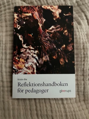 Reflektionshandboken för pedagoger - En bok av Kristin Bie som ger vägledning i reflektion för pedagoger. Omslaget har ett abstrakt mönster i mörka färger och boken är tryckt i mjukt, matt papper. Perfekt för dig som vill utveckla ditt yrkesliv inom utbildning och pedagogik.
