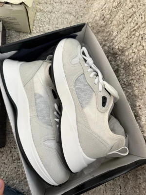 Vita Dior sneakers med meshdetaljer - Helt nya med kvitto samt påse, ett par stilrena vita Dior sneakers med snygga meshpaneler på sidorna och detaljer i mocka. Skorna har vita skosnören och en chunky vit sula med svart undersida. Perfekta för dig som gillar exklusiv och modern streetstyle.