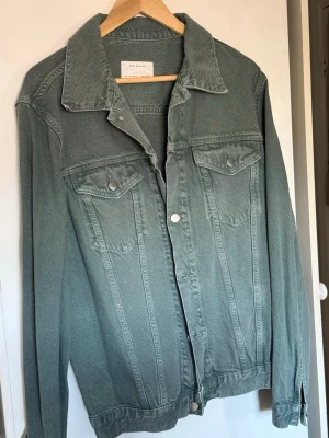 Grön jeansjacka från Zara Man - Snygg grön jeansjacka från Zara Man med klassisk krage, två bröstfickor med lock och silverfärgade knappar. Rak passform och stilrena sömmar framtill. Perfekt för dig som vill ha en enkel men trendig look.