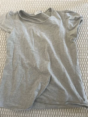 Grå basic t-shirt från Divided - Enkel grå t-shirt från Divided med rund halsringning och korta ärmar. Perfekt till jeans eller shorts för en avslappnad stil. Tillverkad i mjuk bomull för skön känsla hela dagen.