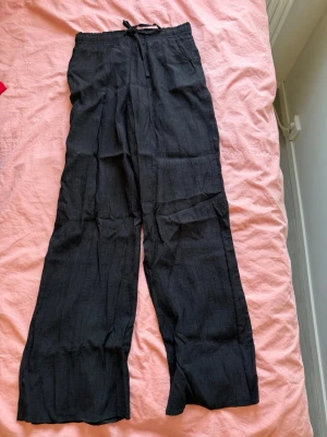 Svarta vida linnebyxor från Zara - Snygga svarta linnebyxor med avslappnad passform och dragsko i midjan. Byxorna har raka, vida ben och är tillverkade i ett lätt och luftigt linnematerial. Perfekta för en chill och stilren look.