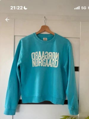 Turkos sweatshirt från Mads Nørgaard - Snygg turkos sweatshirt från Mads Nørgaard med vit spegelvänd logga framtill. Tröjan har rund halsringning, långa ärmar och ribbade muddar vid ärmslut och nederkant. Tillverkad i mjukt bomullsmaterial som är skönt mot huden.