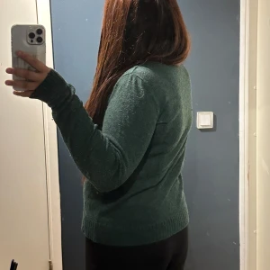 Mörkgrön stickad tröja med v-ringning - Mysig mörkgrön stickad tröja med v-ringad hals och långa ärmar. Tröjan har en klassisk passform och ribbade muddar vid ärmslut och nederkant. Perfekt för lager-på-lager och chill dagar.