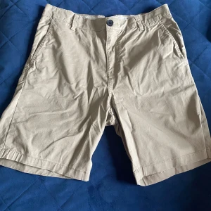 Beige shorts från Selected Homme - Snygga beige shorts från Selected Homme med klassisk passform och bälteshällor. De har fickor fram och bak, stängs med knapp och dragkedja. Perfekta för varma dagar och enkla att matcha med allt. Materialet är mjuk bomull som känns skönt mot huden.