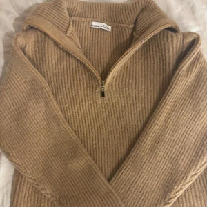 Beige ribbad half zip tröja  - Säljer en beige ribbad stickad tröja från Pull&Bear i storlek XS. Tröjan har en snygg half zip-dragkedja och hög krage, perfekt för att hålla värmen. Materialet är mjukt och grovstickat, vilket ger en chill och trendig look.