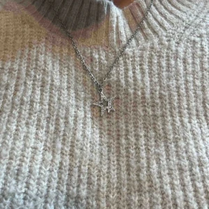 Silverhalsband med glittrande stjärnhänge - Snyggt halsband i silverfärg med ett hänge format som två stjärnor, där den större är dekorerad med små glittrande stenar. Kedjan är tunn. 