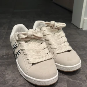 Vita sneakers från din sko, strl 39 - Snygga vita sneakers från Attitude i storlek 39. Skorna har breda vita snören och coola leopardmönstrade detaljer på sidorna. Ovandelen är i syntetmaterial med klassisk rund tå och platt sula. Perfekta för dig som vill sticka ut lite extra. Har använt typ en gång