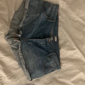 Blå jeansshorts från Roxy, storlek 29 - Snygga blå jeansshorts från Roxy med klassisk femficksdesign och uppvikta benslut. Shortsen har knappgylf och bälteshällor, vilket gör dem perfekta för en chill och avslappnad stil. Materialet är slitstark bomull och passformen är normal.