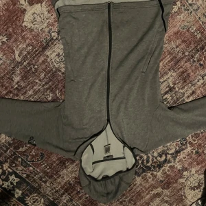 Grå hoodie från Adidas med dragkedja - Säljer en grå hoodie från Adidas i storlek L. Tröjan har hel dragkedja framtill, två fickor och en skön huva. Materialet är mjuk bomull och polyester, perfekt för chill eller träning. Adidas-logga på ärmen för extra stil.