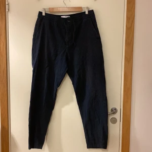 Mörkblå byxor från Selected Homme large  - Snygga mörkblå byxor från Selected Homme med avslappnad passform och elastisk midja. Byxorna har snedställda fickor fram och en bakficka, tillverkade i bomull för en skön känsla. Perfekta för en chill och stilren look. Fint beg skick. Large 