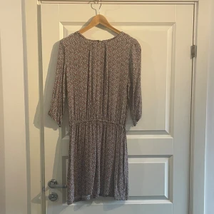 Mönstrad kortklänning Pernilla Wahlgren - Kortklänning från Pernilla Wahlgren med unikt mönster i rostbrunt, blått och vitt. Klänningen har trekvartsärm, resår i midjan och rund hals med knapp i nacken. Lätt och skönt material.
