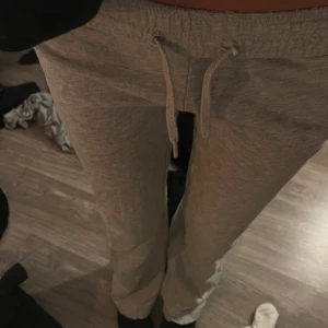 Grå mjukisbyxor med snörning - Säljer ett par grå mjukisbyxor med dragsko i midjan. Byxorna har en avslappnad passform och är tillverkade i mjukt bomullsmaterial. Perfekta för chill dagar hemma eller när du vill vara bekväm. Klassisk look med raka ben och elastisk midja.