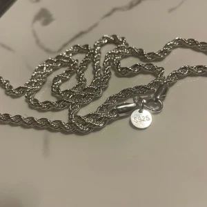 Cordell halsband 925 silver platering 4mm 60 och 50cm finns - Säljer ett snyggt halsband i  925 silver platering med tvinnad kedja som ger en cool och stilren look. Perfekt för dig som vill ha ett statement-smycke som syns. Kedjan har en rund bricka med 925-stämpel och robust lås.