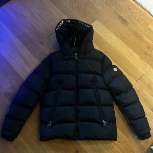 Svart Moncler pufferjacka med huva - säljer min svarta pufferjacka från Moncler med stor huva och tydlig logotyp på huvkanten. Jackan har aldrig kommit till användning så den är som ny. 