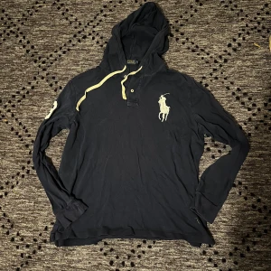 Mörkblå hoodie från Ralph Lauren - Snygg mörkblå hoodie från Polo Ralph Lauren med stor vit logga på bröstet och siffran 3 på ärmen. Tröjan har huva med ljusa snören och knappar vid halsen. Storlek L passar M