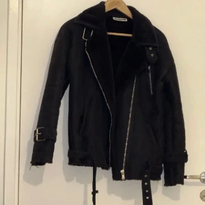 Noisy may - Svart teddyjacka med grov krage, silvriga dragkedjor och spännen vid ärmslut och krage. Jackan har ett bälte nedtill och är fodrad med mjuk teddy på insidan. Perfekt för kalla dagar med sin oversized look och coola detaljer.