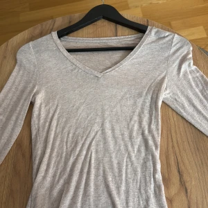 Intimissimi topp långärmad - Säljer en stilren beige långärmad topp med v-ringad hals. Toppen har en mjuk och tunn känsla, perfekt för lager-på-lager. Passformen är normal och materialet känns som bomull eller en bomullsblandning. Enkel design som funkar till många olika looks.