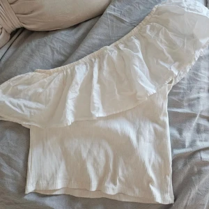 Vit offshoulder topp med volang - Säljer en superfin vit offshoulder topp med bred volang runt axlarna. Från zara tror jag strl S. Lite sminkfläckar längst upp (2a bild) men går såklart fort i tvätten🥰