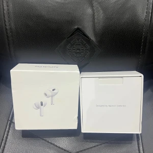 AirPods Pro 2 - Apple AirPods Pro i originalförpackning med laddningsetui, extra öronproppar, laddkabel och dokumentation. Allt ser komplett ut och i mycket gott skick. Perfekt för brusreducering och trådlös musikupplevelse. Kartongen har några mindre skavanker.