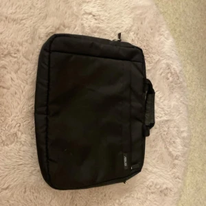 Svart datorväska från ASUS - Svart datorväska från ASUS med stilren och enkel design. Väskan har ett vadderat fack för laptop, praktiskt handtag och dragkedja upptill. Tillverkad i slitstark polyester och passar perfekt för att bära med sig dator och tillbehör.