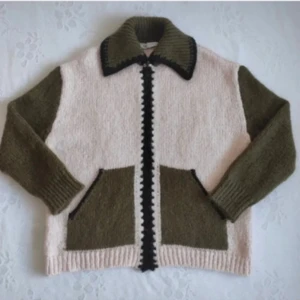 Stickad cardigan jacka med fickor - Säljer en stickad cardigan jacka i beige och olivgrönt med svarta detaljer längs dragkedjan och kragen. Jackan har två stora fickor framtill och ribbade muddar vid ärmslut och nederkant. Perfekt för dig som gillar retrovibbar och mysiga material.
