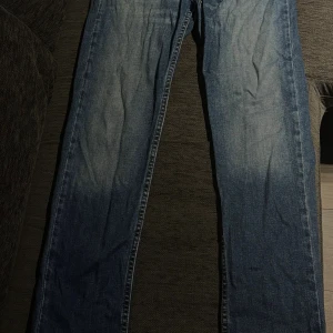 Blå raka jeans i klassisk modell - Säljer ett par blå jeans med klassisk rak passform och normal midja. Jeansen har fyra fickor, snygga slitningar och kontrastsömmar. Perfekta för dig som gillar en tidlös stil och vill ha ett par jeans som funkar till det mesta. 